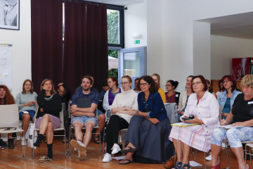Pozorní účastníci sedí v sále na židlích a sledují probíhající program